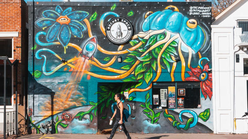 Man walking in front of store front mural.